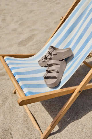Beige sandal on a striped deck chair on sandy ground